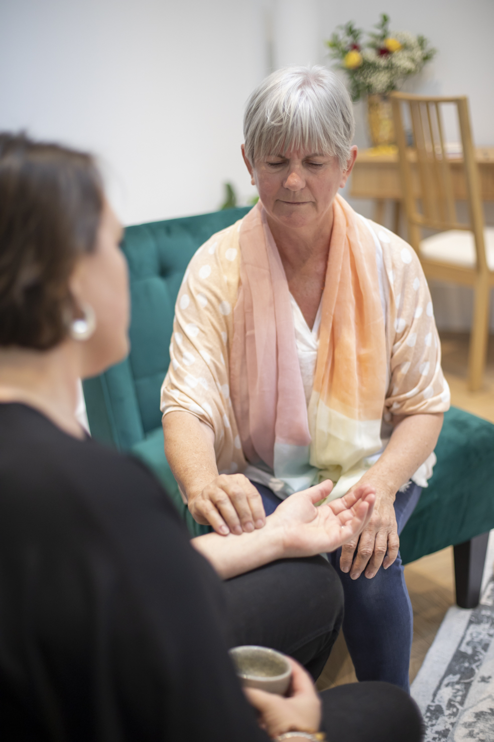 Radha checking a students pulse with her fingers placed on the forearm of her student inside the yoga studio